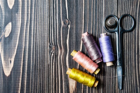 Accessories for sewing on dark wooden table - thread, scissors. Copy space.