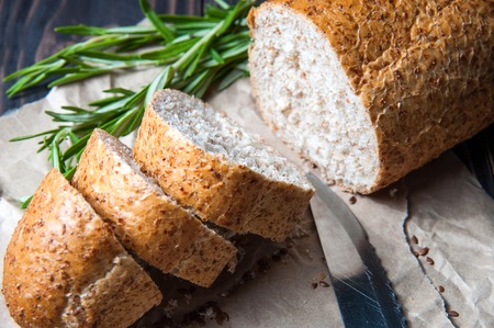 Homemade sliced bread with knife, herbs and seeds on cooking paper