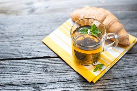 Fresh baked croissants with mint tea on yellow napkin. Wooden table.の写真素材