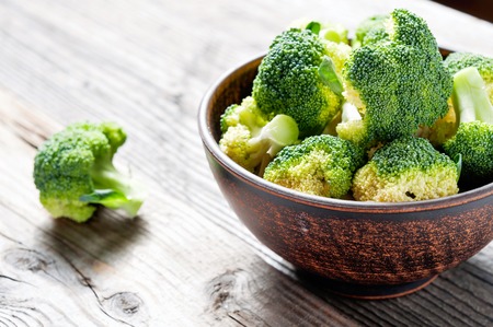 Broccoli cabbage pieces in a clay bowl on a wooden background, product for vegan dishes.