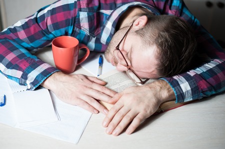 Businessman in casual cloth sleeping at the table with book and papers in office top view
