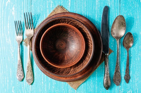 Brown plates with vintage cutlery on blue rustic wooden table, top view
