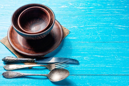 Still life with brown rustic ceramic plate and old cutlery set on blue wooden table with copy spaceの写真素材