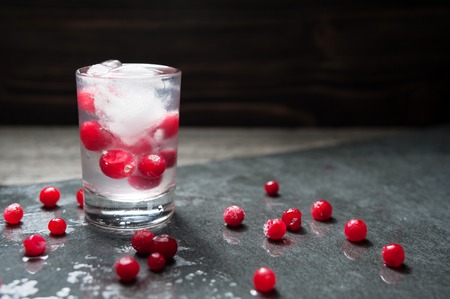 close-up with fresh cranberries, glass of Russian vodka and ice cubes on black background water dropsの写真素材