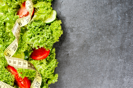 Sport and diet. Vegetables. Measuring tape, cucumber, tomatoes, salad on dark stone background. Top view with copyspace,の写真素材