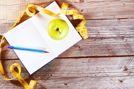 Blank open notebook with green apple and yellow centimeter tapeand pen. Concept sport, diet, fitness, healthy eating. Top view, copyspace, toned.の写真素材