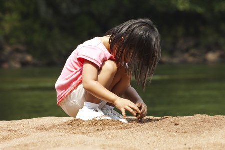 Asian toddler playing in the sand of a river bankの写真素材