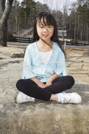 portrait of a young Asian girl sitting on rocksの写真素材
