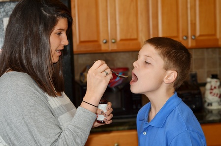 Adult is giving a young boy medicine by spoonの写真素材