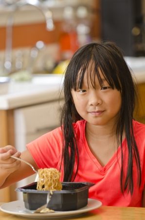 Cute young Asian girl with a fork full of noodlesの写真素材