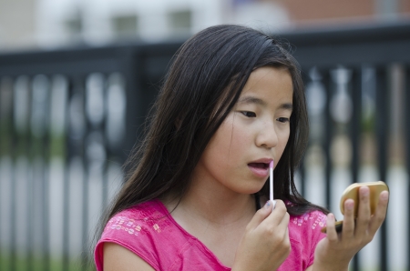 Pretty young Asian girl concentrating on applying lip glossの写真素材