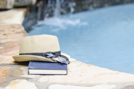 hat, glasses and a book by the pool sideの写真素材
