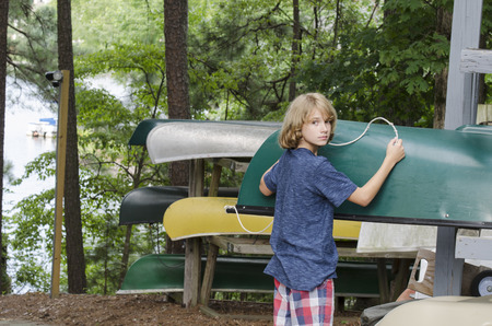 Young boy loading a canoe onto the storage rack at campの写真素材