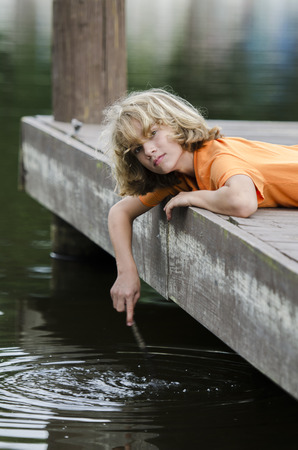 boy stirring the water surface with a stickの写真素材
