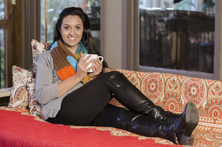 Pretty young Indian woman sitting back with a cup of teaの写真素材