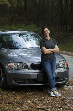 Happy woman leaning against her car on a counry roadの写真素材