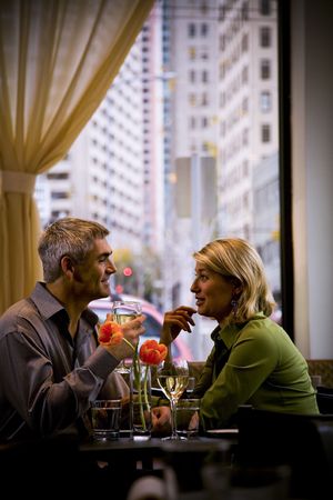 A couple sits at a small cafe table, drinking wine. Vertically framed shot.の写真素材