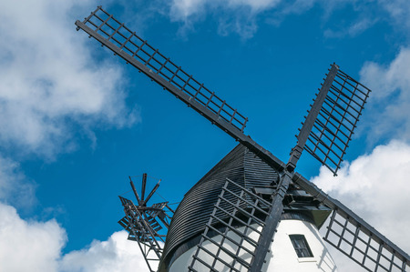 Windmill close up, with black sails ,wooden slatted roof against blue sky with fluffy white cloudsの写真素材