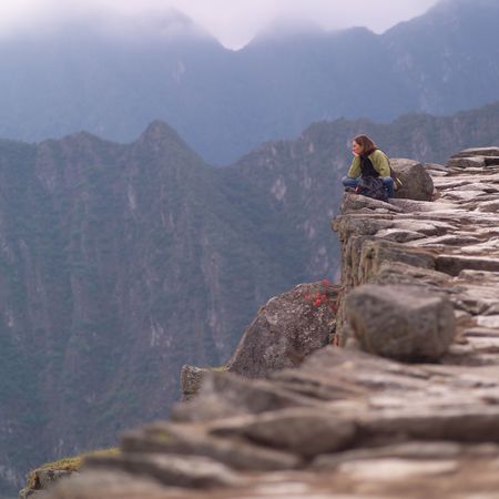 Peru - Machu Picchu, Woman sitting on the edge of a mountainの写真素材