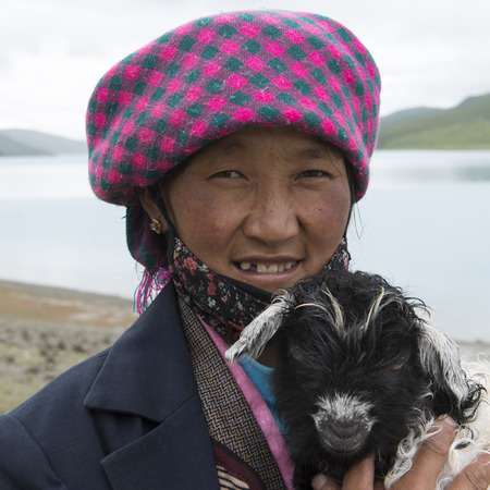 Woman holding a lamb at the lakeside, Yamdrok Lake, Tibet, Chinaのeditorial素材