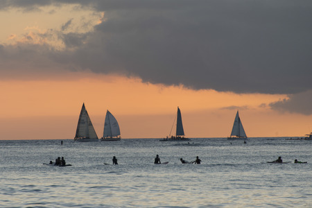 Surfers on the beach with sailboats in the background at sunset, Waikiki, Honolulu, Oahu, Hawaii, USAのeditorial素材
