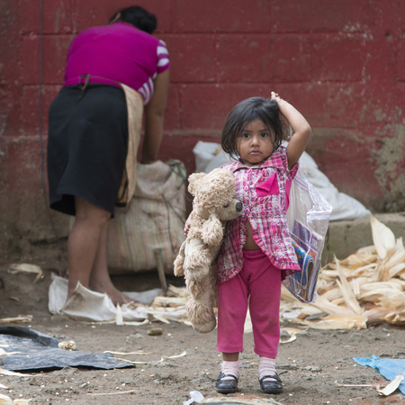 Girl holding a toy with her mother working in background, Finca El Cisne, Hondurasのeditorial素材