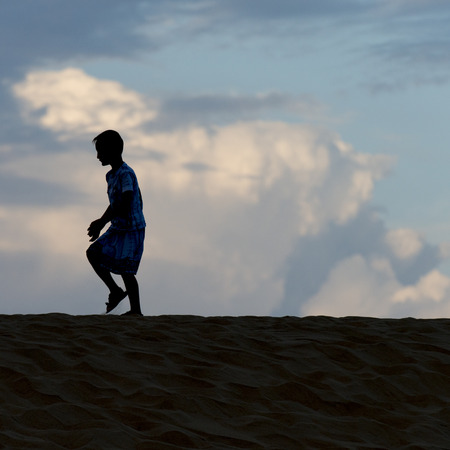Boy walking on sand dune at Mingsha Shan, Dunhuang, Jiuquan, Gansu Province, Chinaの写真素材