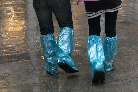Low section of couple wearing plastic rain shoes walking on sidewalk, Venice, Veneto, Italyの写真素材