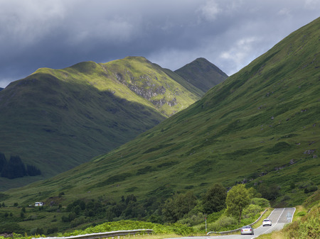 Cars moving on a mountain road against cloudy sky, Scottish Highlands, Scotlandの写真素材