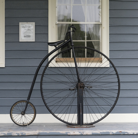 Penny farthing bicycle against house on sidewalk, Sherbrooke, Nova Scotia, Canadaの写真素材
