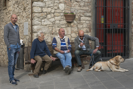 Men sitting on bench with dog on street by building, Radda in Chianti, Tuscany, Italyのeditorial素材