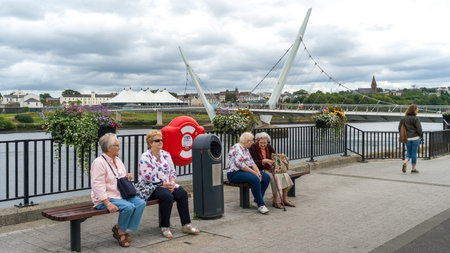 Tourists resting on benches on sidewalk, The Peace Bridge, Londonderry, Northern Ireland, United Kingdomのeditorial素材