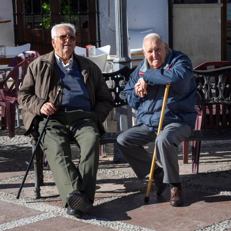 Old male friends sitting on bench, Plaza Del Socorro, Ronda, Malaga, Andalusia, Spainのeditorial素材