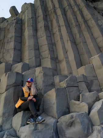Woman sitting on basalt rock, Reynisfjara Black Sand Beach, Vik, Myrdalshreppur, Southern Region, Icelandのeditorial素材