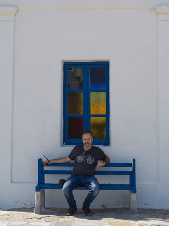 Male tourist seated on a blue bench on Mykonos Island, Greeceのeditorial素材