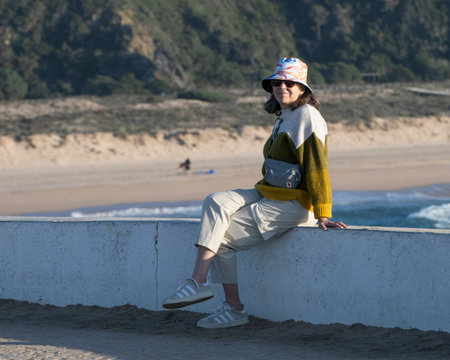 Female tourist sitting on a ledge along the coast of Farol de Milfontes Rio Mira, Beja, Portugalのeditorial素材