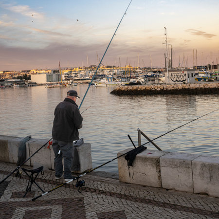 Man fishing off the pier along the shoreline of Lagos which is a town in southern Portugal's Algarve region. Itâs known for its walled old town, cliffs and Atlantic beachesのeditorial素材