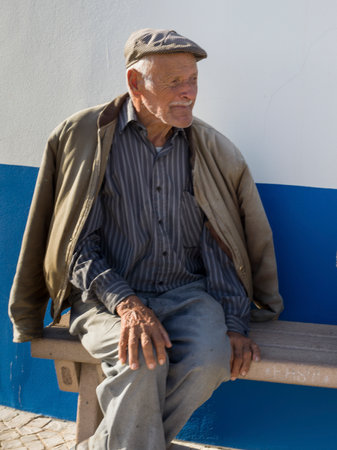 Senior elderly man sitting on a bench in a village in Portuga that lies on the south bank of the Ribeira de Seixe, which here forms the border between the Algarve and Alentejo, Odeceixe, Faro, Portugalのeditorial素材
