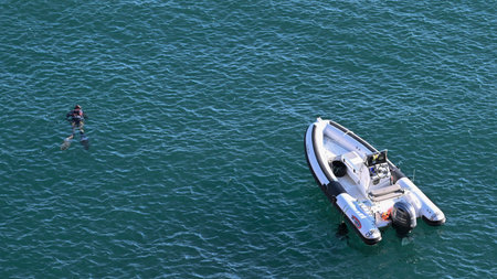 Swimmer in the ocean alongside a boat in the ocean, off the coast of Segres, Faro, Portugal, that sits at the extreme western tip of the Algarveのeditorial素材
