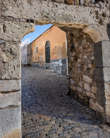 Stone archway along a cobblestone street in Faro which is the capital of southern Portugalâs Algarve region. The cityâs neoclassical Arco da Vila is on the site of a gate that was part of the original Moorish wallのeditorial素材