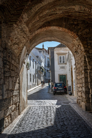 Cobblestone narrow rode in Faro that is the capital of southern Portugalâs Algarve region. The cityâs neoclassical Arco da Vila is on the site of a gate that was part of the original Moorish wallのeditorial素材