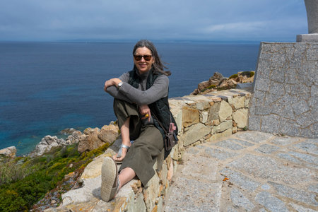 Female tourist sitting on a stone wall that overlooks the coastline, Santa Teressa Gallura, Sassari, Sardinia, Italyのeditorial素材
