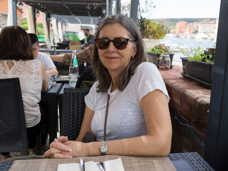 Woman wearing sunglasses seated at an outdoor dining area, Town of Bosa, Sardinia, Italyのeditorial素材