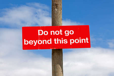 A sign reading â€œDo not go beyond this pointâ€ seen against a largely blue sky.
