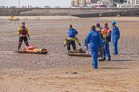 Weston-super-Mare, UK - July 16, 2018: Coastguards rescue a casualty from soft mud on the beach