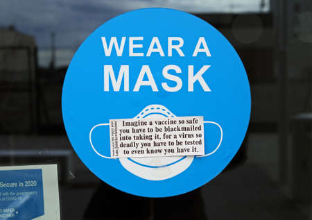 Weston-super-Mare, UK - April 9, 2021: A sticker promoting conspiracy theories about COVID-19 placed on a sign encouraging the wearing of masksのeditorial素材