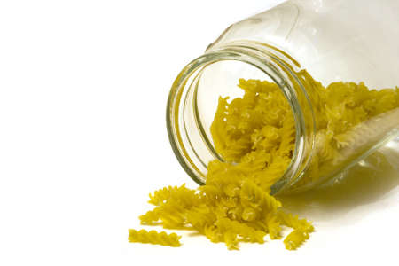 mound of fusilli pasta falling out of a large jar onto a white surfaceの写真素材