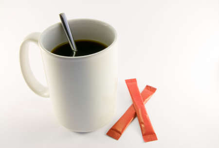 Tall white coffee mug with two red sugar sachets and spoon on a white backgroundの写真素材