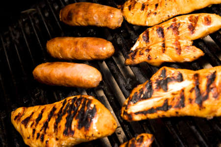 Five pieces of chicken and sausages cooking on the barbequeの写真素材