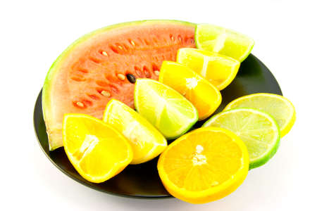 Slice of juicy red watermelon with lemon, lime and orange wedges and slices on a black plate with a white backgroundの写真素材